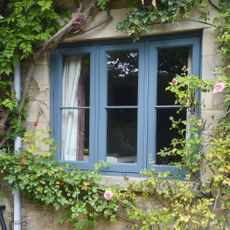 traditional windows blue accoya windows in stone building with climbing roses and wisteria