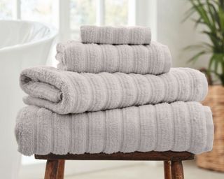 DUSK Monaco Supreme Cotton Towels in grey, folded sitting on wooden stool and stacked