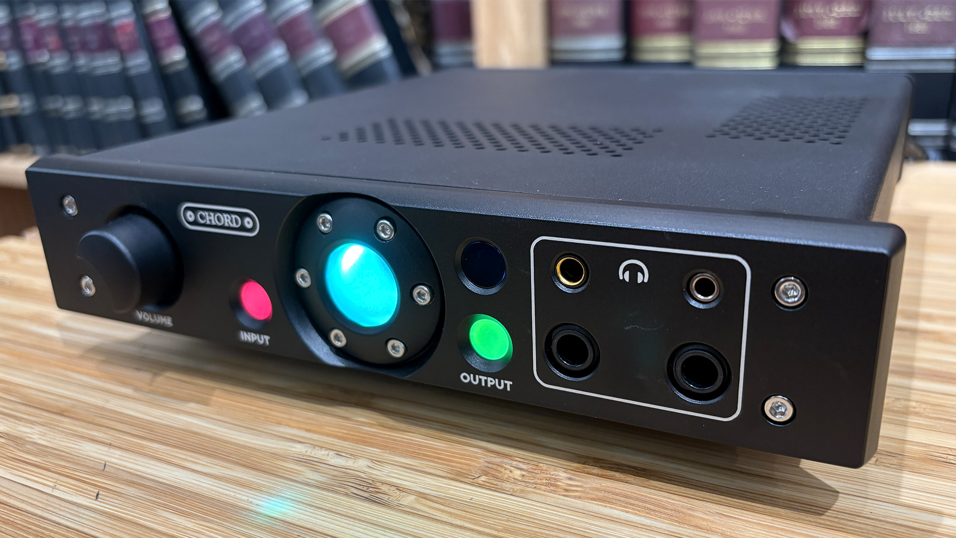 Chord Electronics Alto headphone amp on wooden surface showing front panel lights and controls