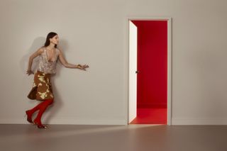 Model in colourful, eclectic outfit walks through a door to a red room wearing looks from the S/S 2025 season