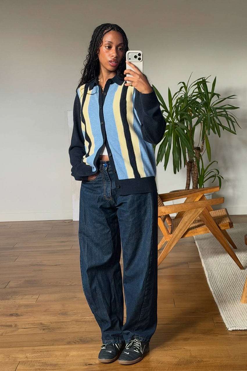 a woman wearing a blue, yellow, and black sweater, indigo jeans, and black Nike sneakers