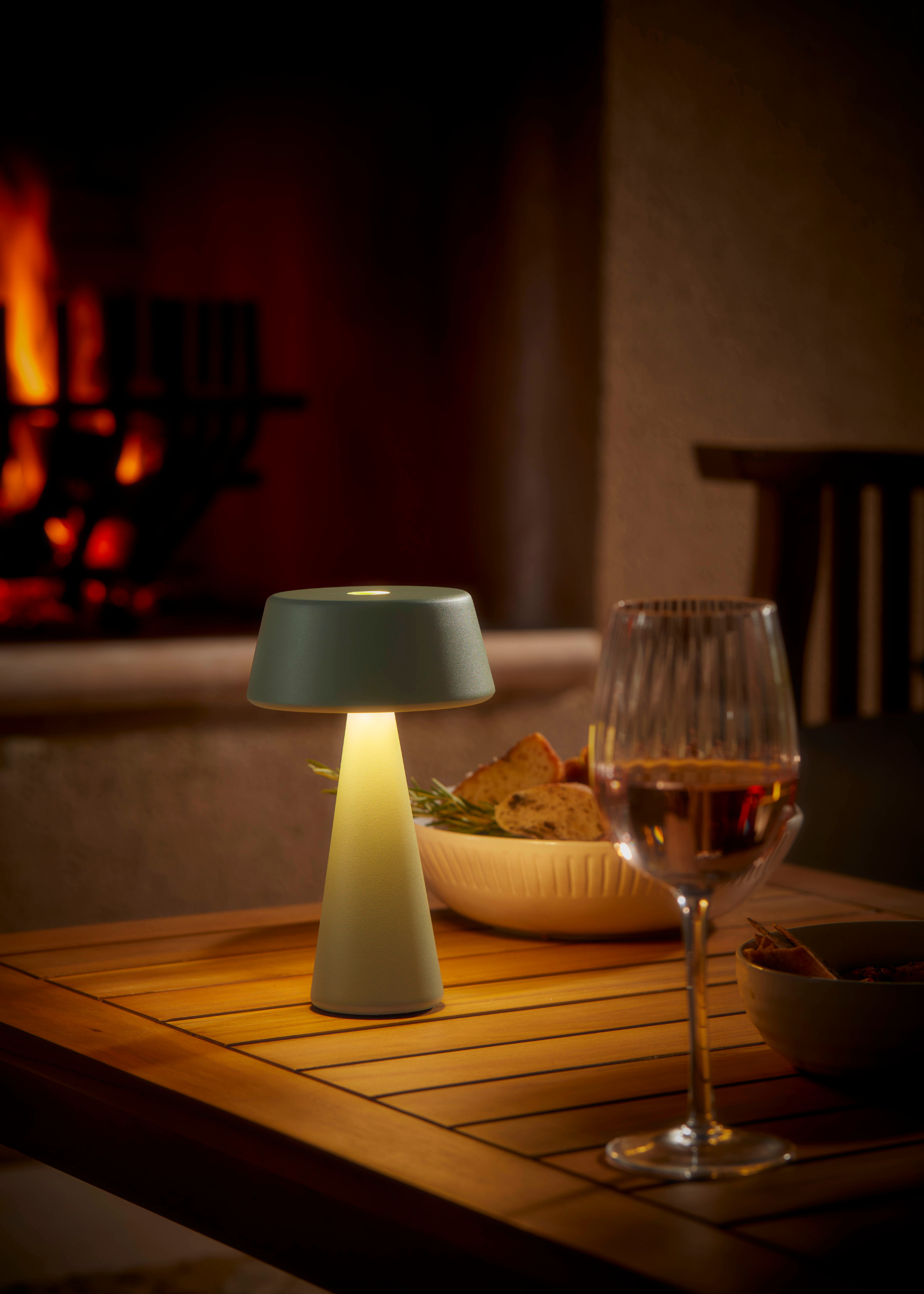 an outdoor wireless table lamp on a wooden table with a glass of wine