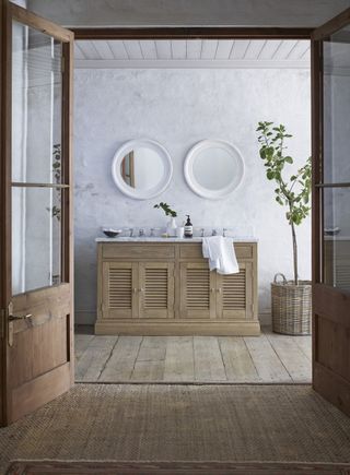An example of traditional powder room ideas showing a wooden washstand below two round mirrors