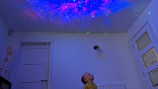 A photo of young toddler enjoying the astronaut starry sky projector nebula patterns.