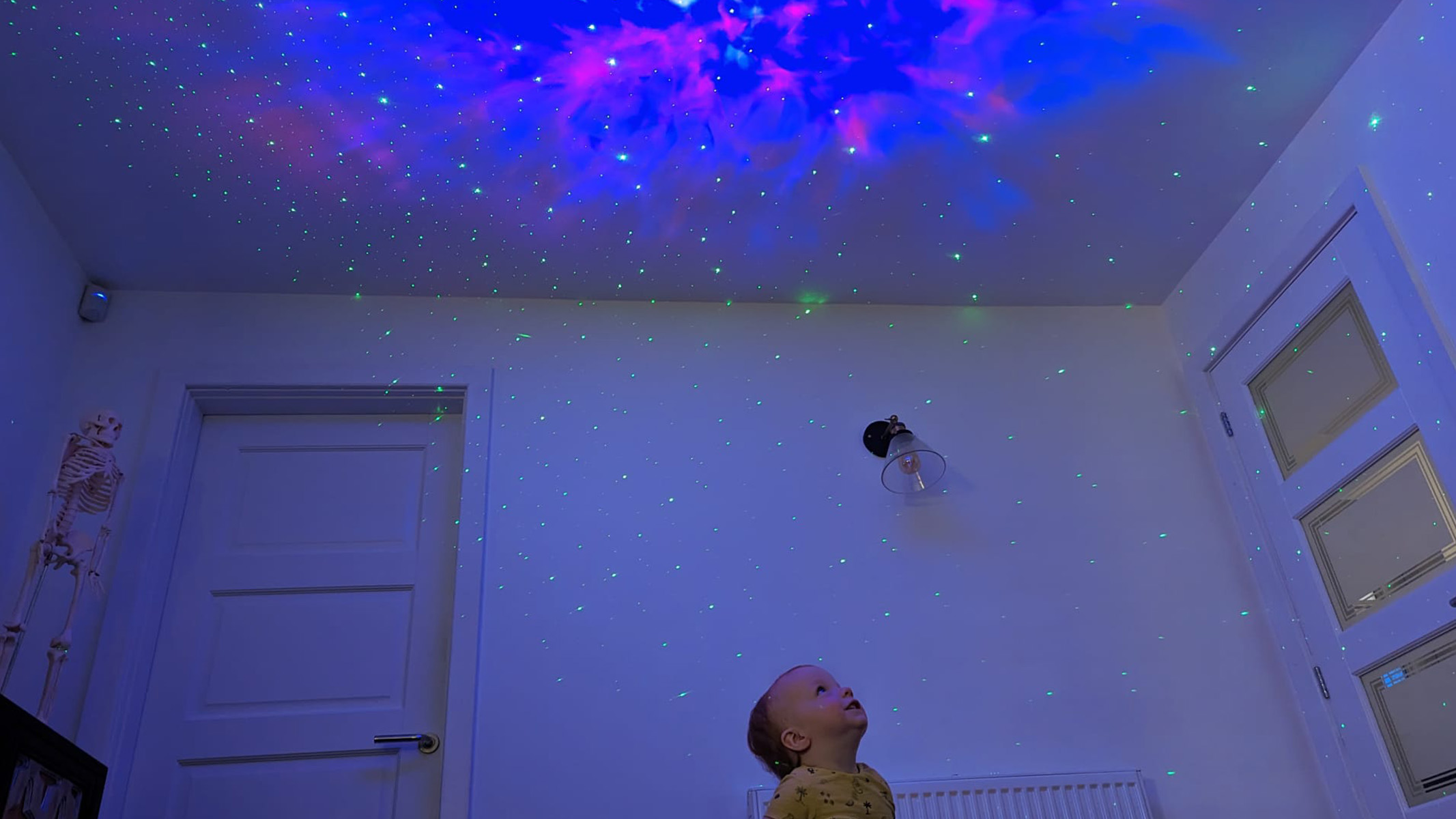 Ein Foto des jungen Kleinkindes, das die sternenklaren Himmelprojektor-Nebelmuster des Astronauten genießt.