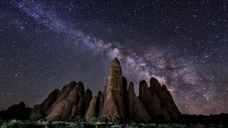 photography of a rock formation appearing to look like several "fins" sticking up out of the ground and pointing up to the starry sky where the Milky Way is visible streaking across the sky.