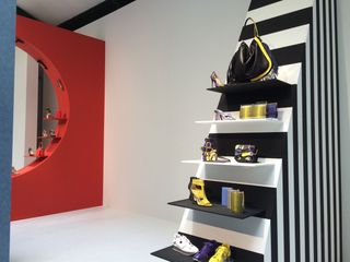Black and white display unit decorated with shoes and handbags across a red cutout drywall decorated with more shoes and handbags