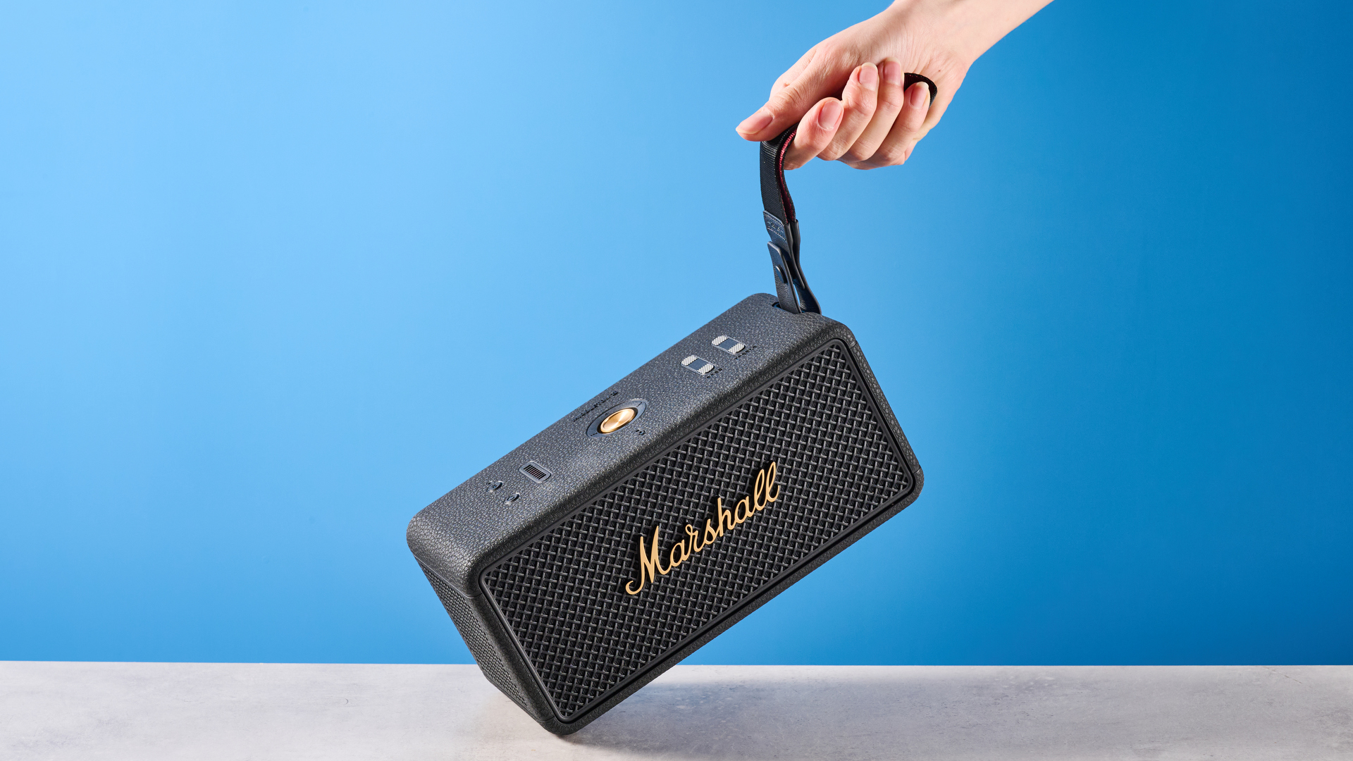 The Marshall Middleton II Bluetooth speaker in Black and Brass, on a stone surface with a blue wall in the background