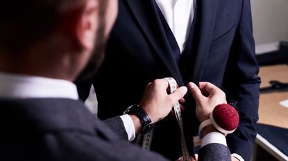 Over-the-shoulder view of a tailor fitting a suit on a man.