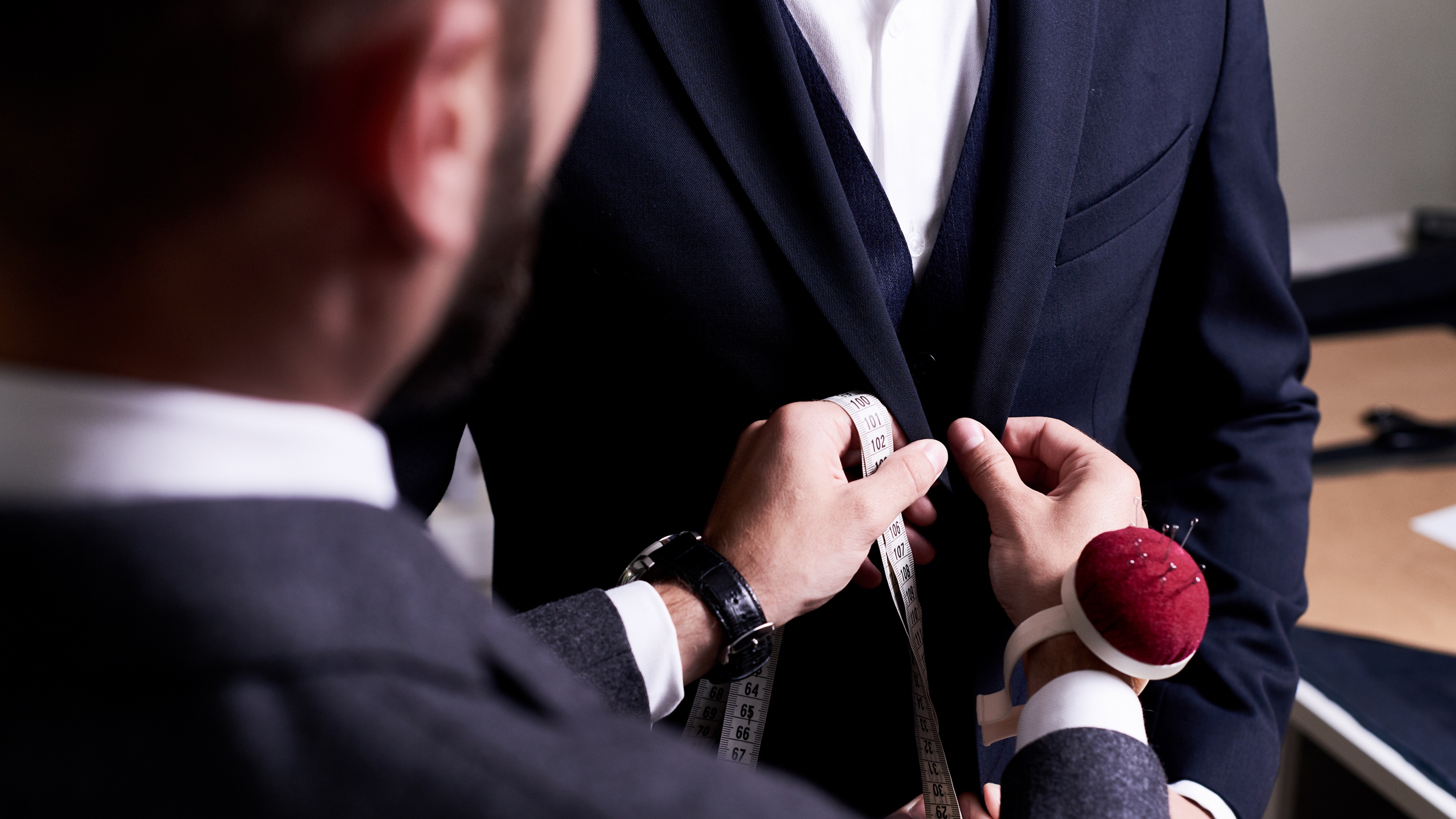 Over-the-shoulder view of a tailor fitting a suit on a man.