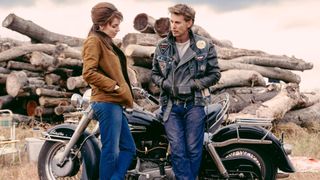 Jodie Comer and Austin Butler stand against a motorbike in The Bikeriders