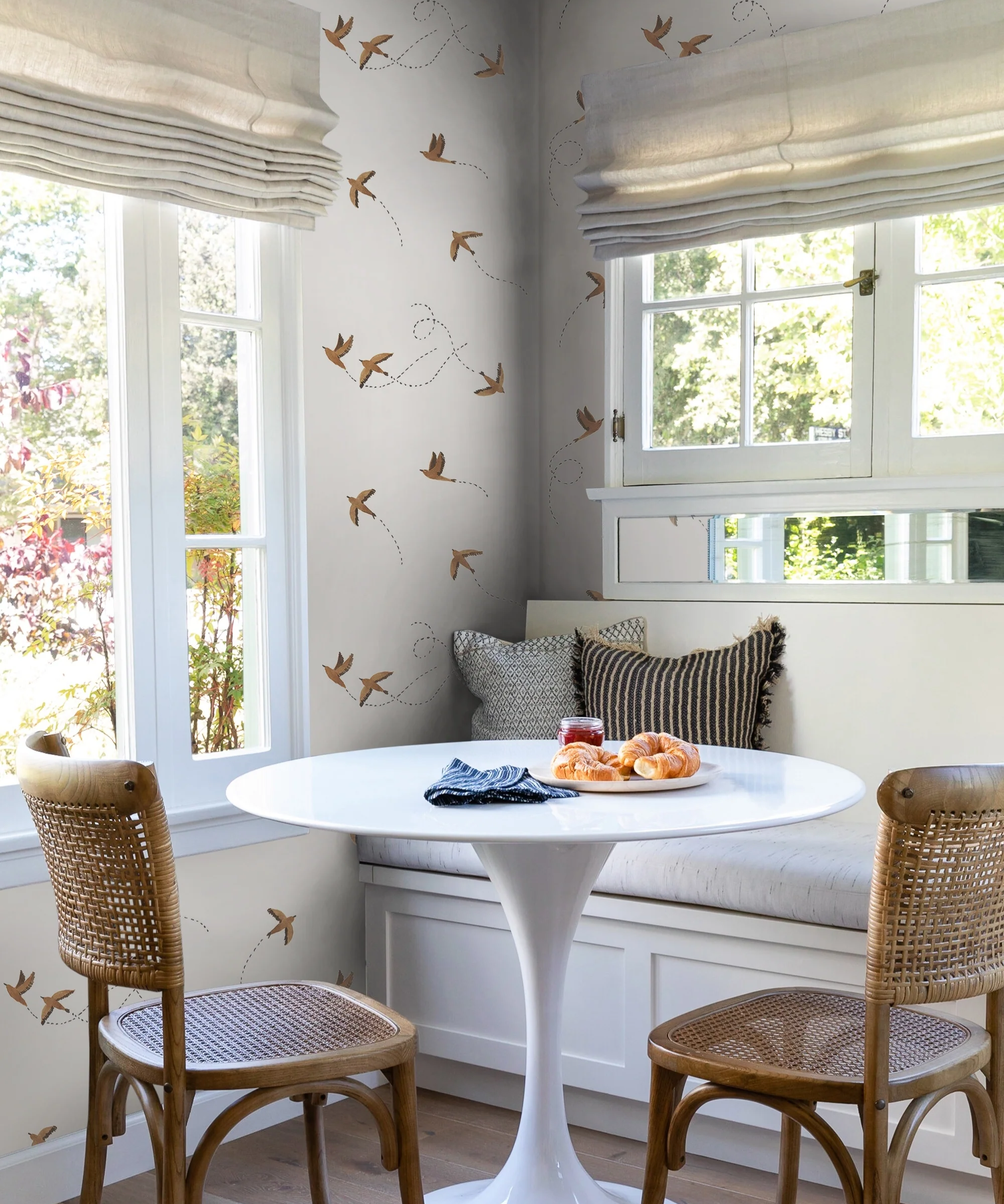 a dining nook with a round table, two chairs, a built in bench, and flying bird wallpaper