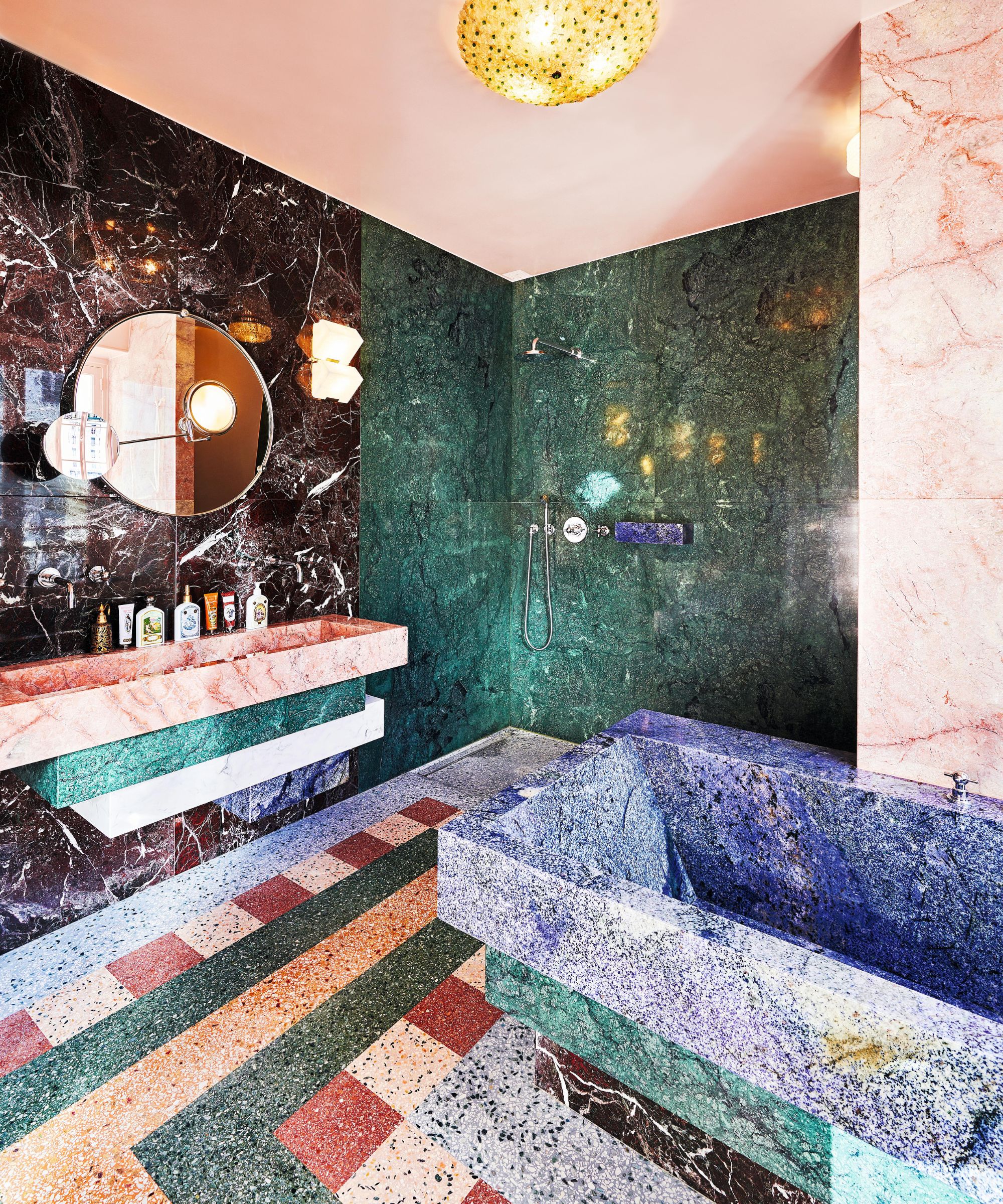 a bold mixed marble bathroom with a green marble shower, blue bathtub and a pink painted ceiling