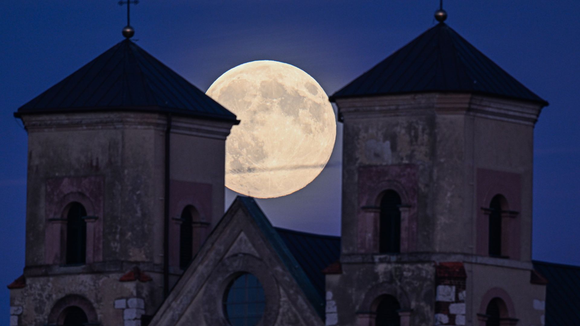 A full moon rises between the towers of an old abbey at night.