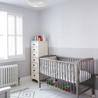 SOft grey walls, white chest of drawers, grey cot, white radiator and large window
