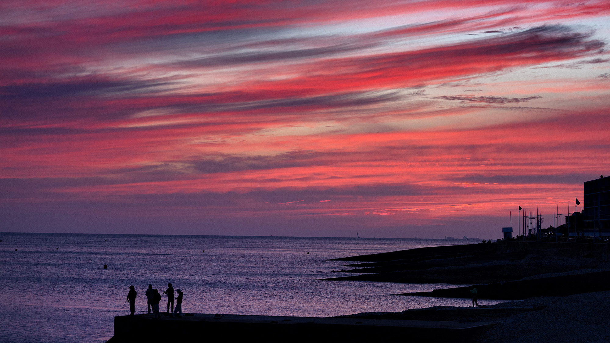 People stand on the jetty as they fish at sunset in Le Havre, France