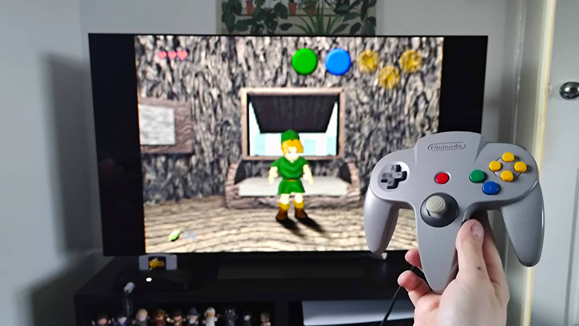 Analogue 3D connected to LG OLED C4 TV with hand holding original grey controller and Zelda: Ocarina of time gameplay in backdrop.