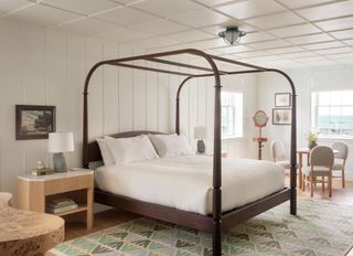 Bedroom interior at Canoe Place Inn. A four pillar connected bed frame with white linen.