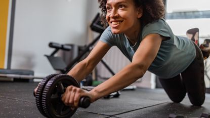 A smiling woman uses an ab wheel