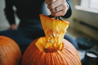 A hand pulling the top of a pumpkin off by the stalk