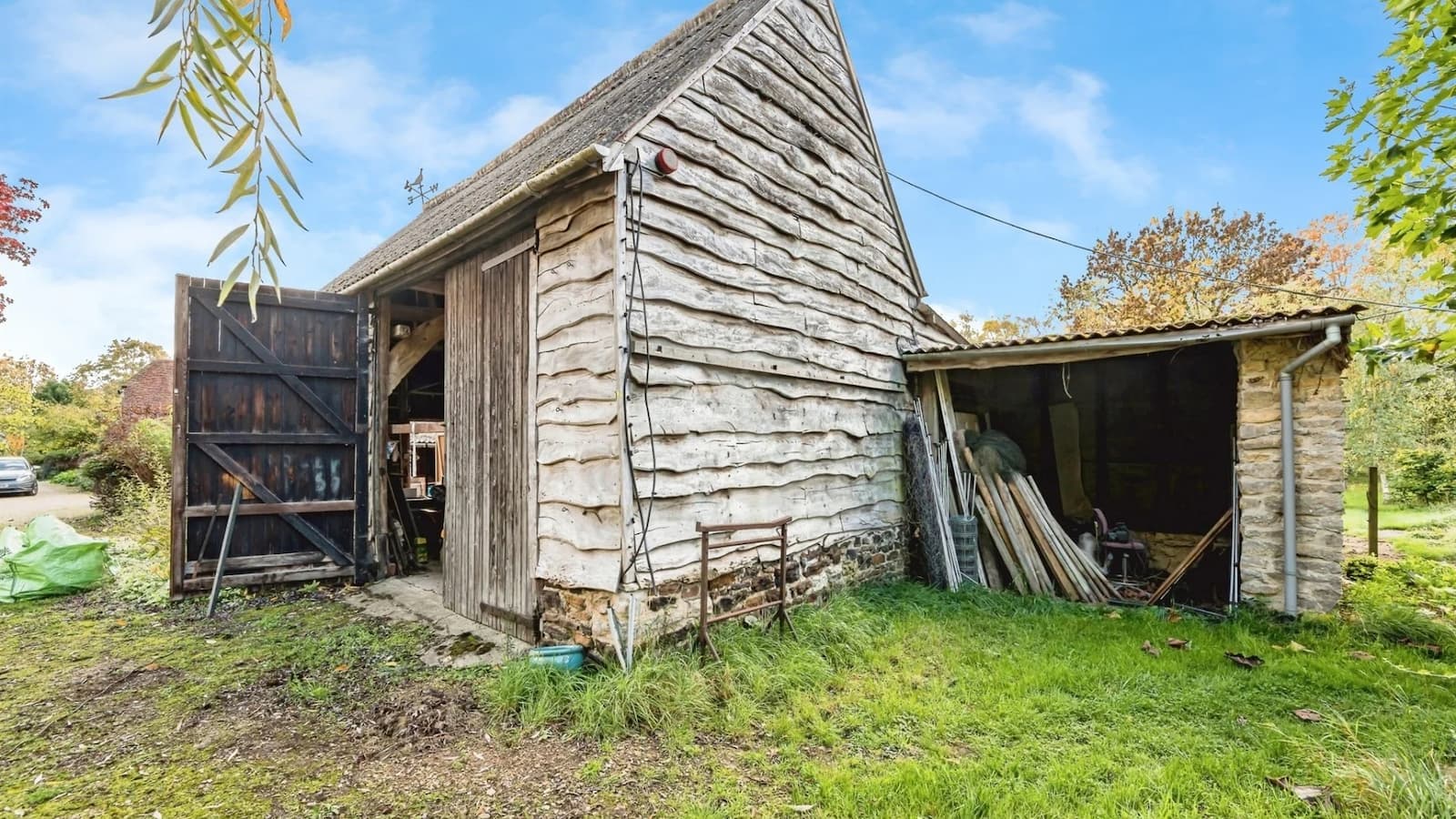 A barn with wooden cladding surrounded by grass and a side outbuilding with scrap inside