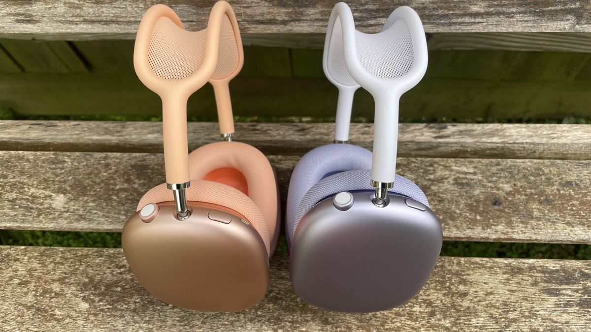Apple AirPods Max 2 in orange with AirPods Max just visible in purple, outside in a garden on a bench, held in a hand