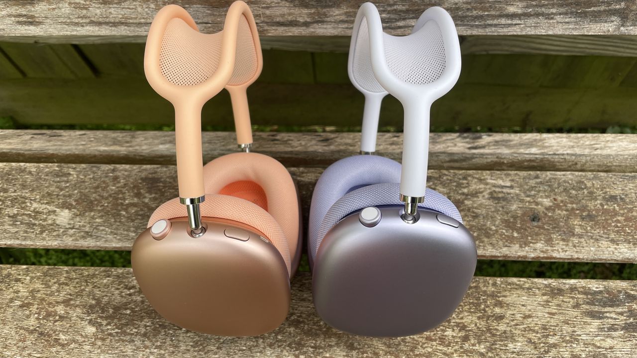 Apple AirPods Max 2 in orange with AirPods Max just visible in purple, outside in a garden on a bench, held in a hand