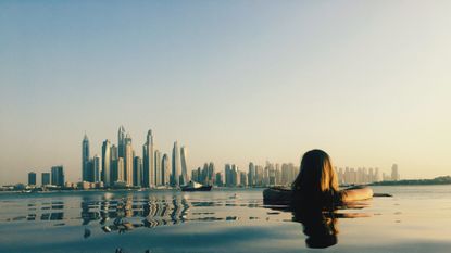 Rear View Of Woman Looking At Modern Building While Swimming In Infinity Pool Against Clear Sky During Sunset