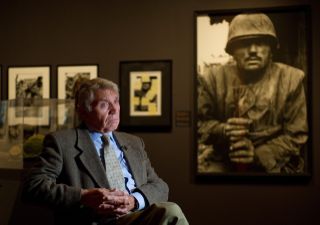 Don McCullin sitting next to one of his famous photos, Shell-shocked Marine