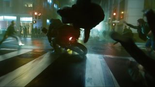 Neo and Trinity ride a motorcycle through a battling crowd in The Matrix Resurrections.