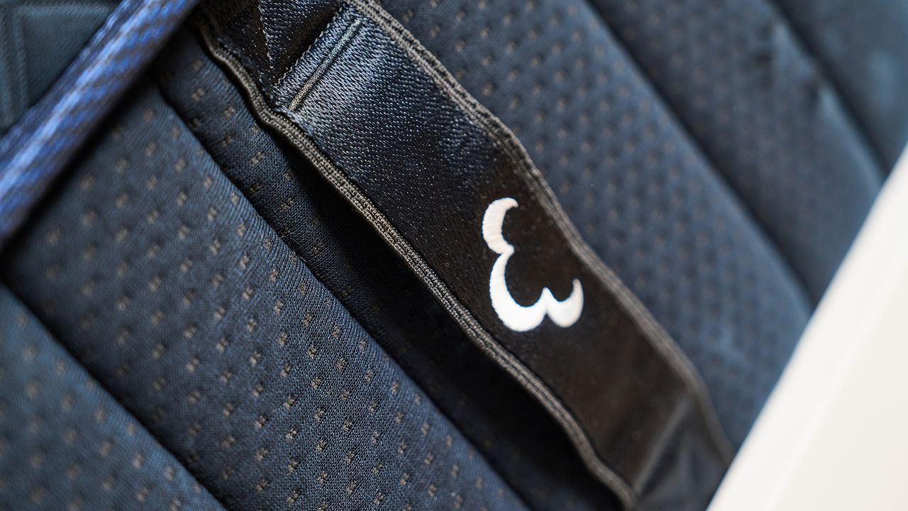 The image shows the close-up details of the DreamCloud Ultra Hybrid, a navy blue mattress placed on a white bed frame in a neutrally decorated bedroom