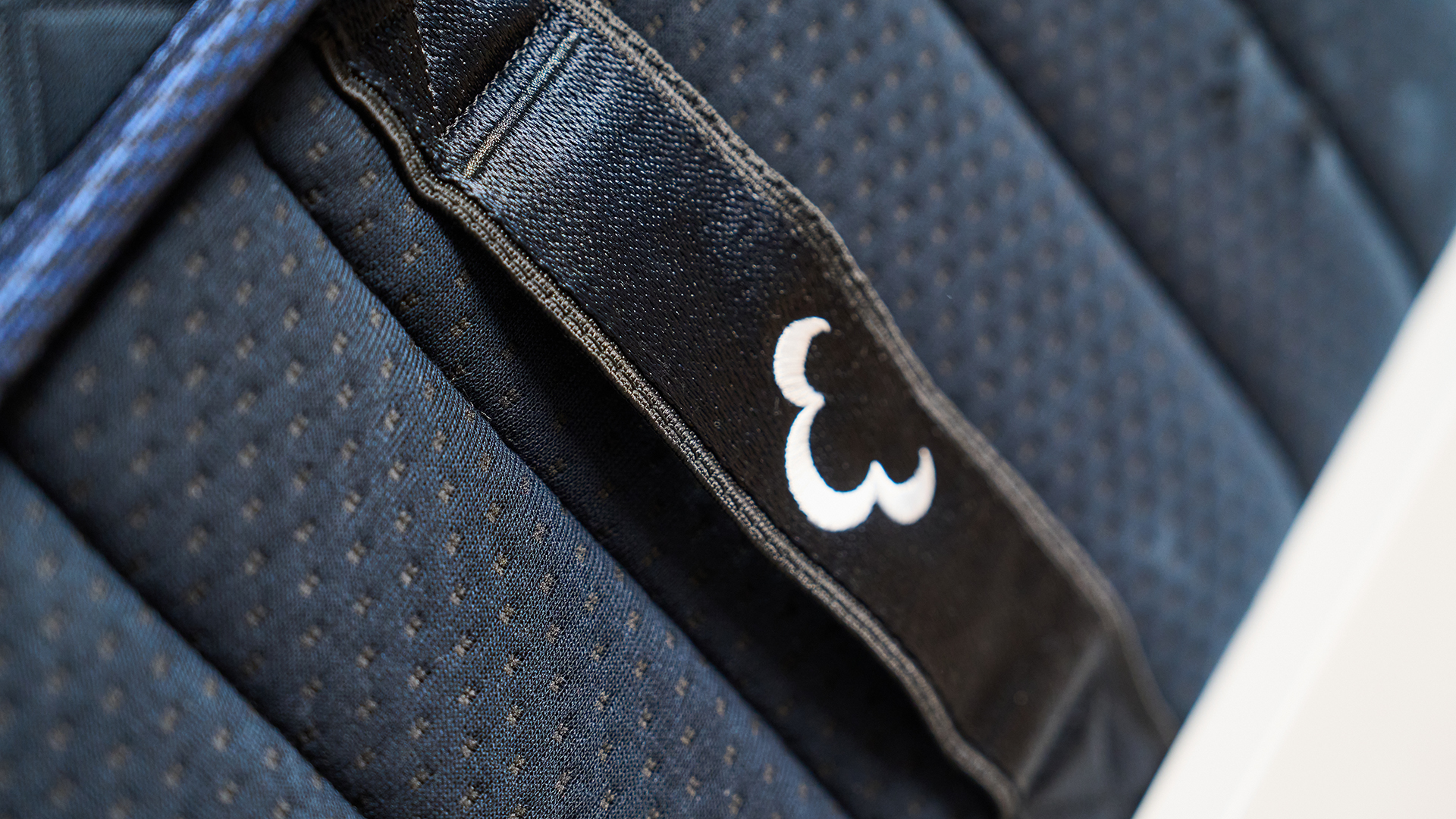 The image shows the close-up details of the DreamCloud Ultra Hybrid, a navy blue mattress placed on a white bed frame in a neutrally decorated bedroom