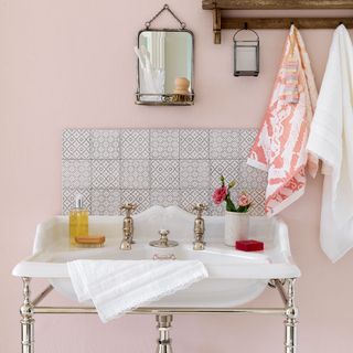 bathroom sink with chrome pipe stand, with a small patterned tile splashback and a small mirror with shelf above, in a bathroom with blush pink walls