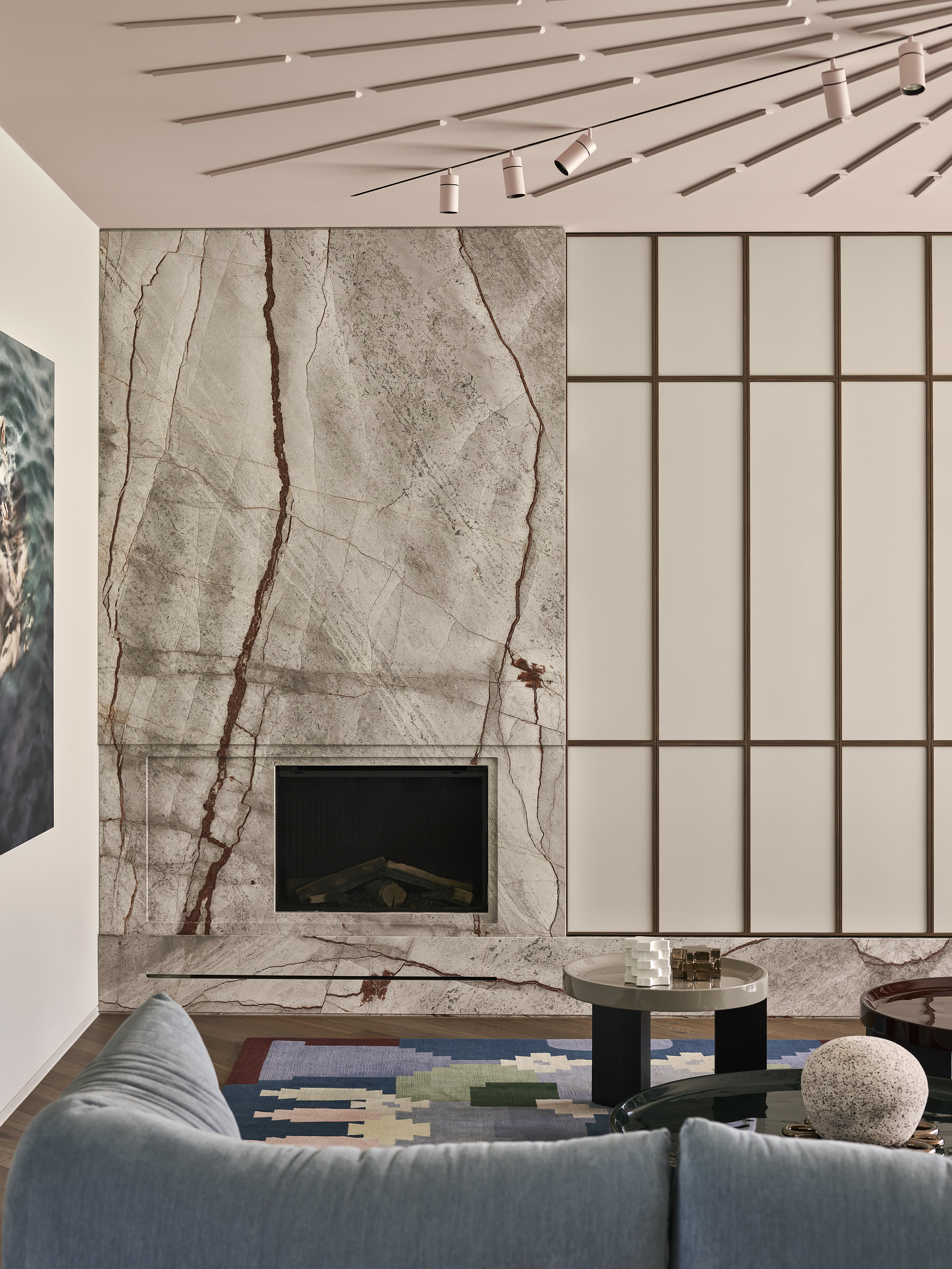 modern living room with marble wall, joinery, pink ceiling with decorative detail, blue sofa, and colorful rug