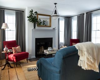 living room with white walls, blue sofa, red chairs, fireplace, gray curtains and wooden floor