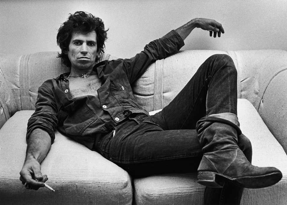 Keith Richards sprawled on a sofa in 1980, cigarette casually dangling between his fingers