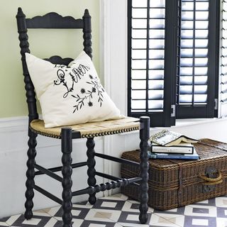 cream hallway with white trim and black window frame with a geographic floor tile and wooden chair with cushion