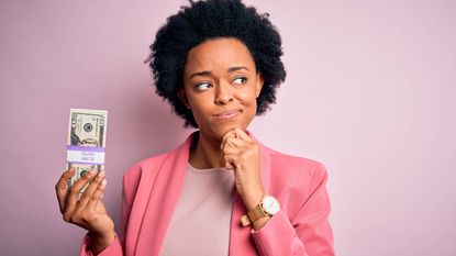 A woman holds $2,000 in a stack of $20s and ponders.