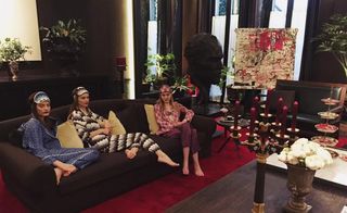 Models sitting on a sofa wearing silk printed pajamas and sleep accessories