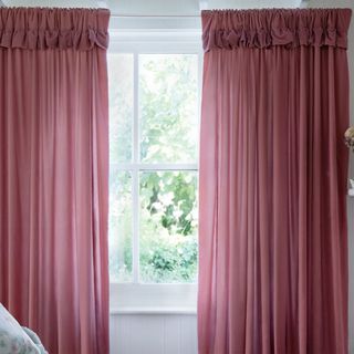 Dark pink curtains hung at a white sash window with greenery behind