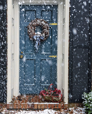 front door of traditional home decorated for christmas with snow