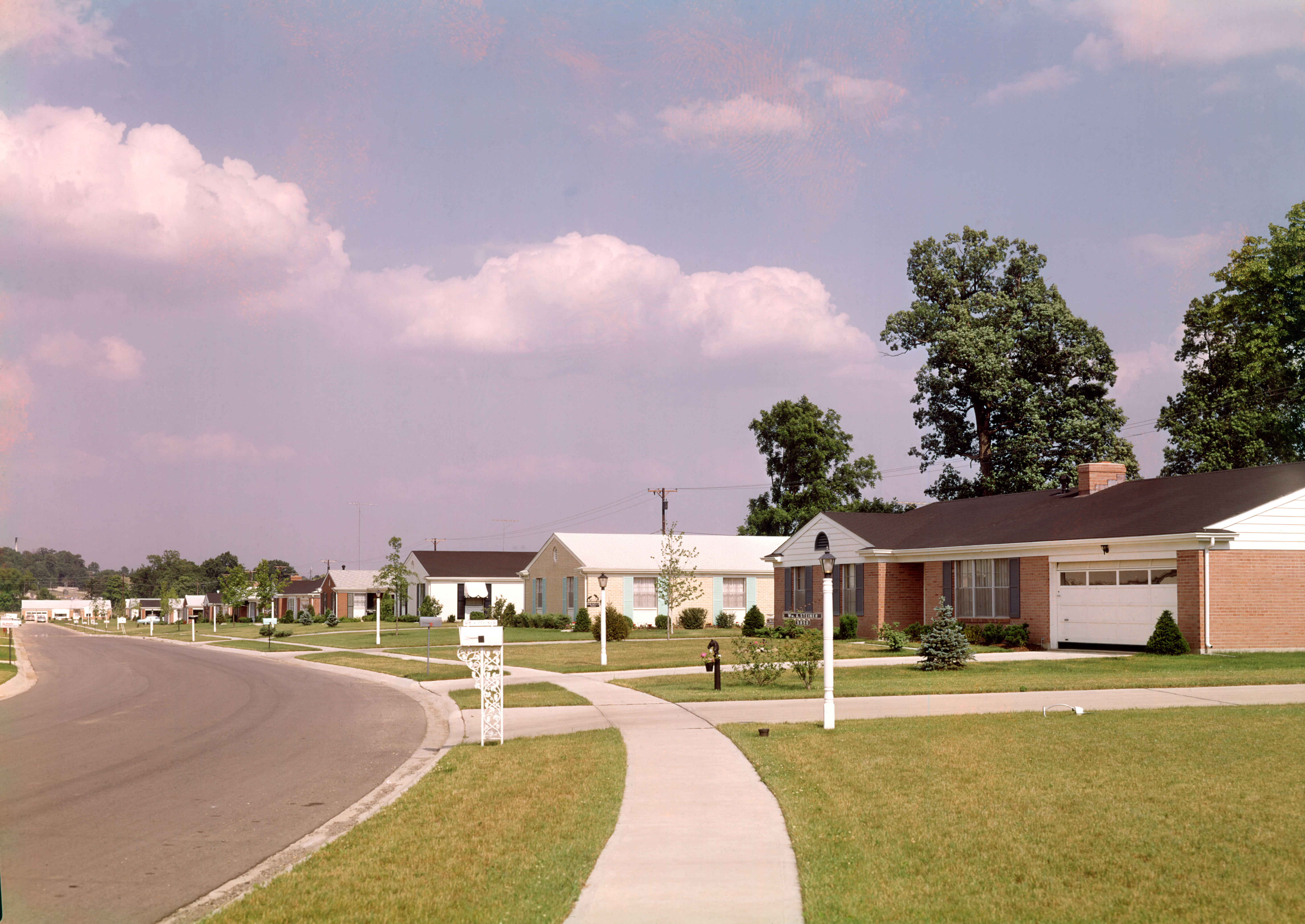 A suburban neighborhood ca. 1960s or 1970s with tidy lawns and no cars.