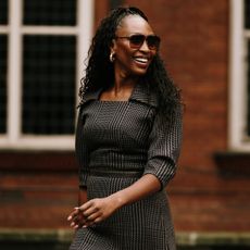 a london spring 2025 fashion week attendee smiling and wearing a checkered dress and sunglasses 
