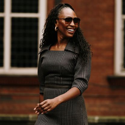 a london spring 2025 fashion week attendee smiling and wearing a checkered dress and sunglasses 