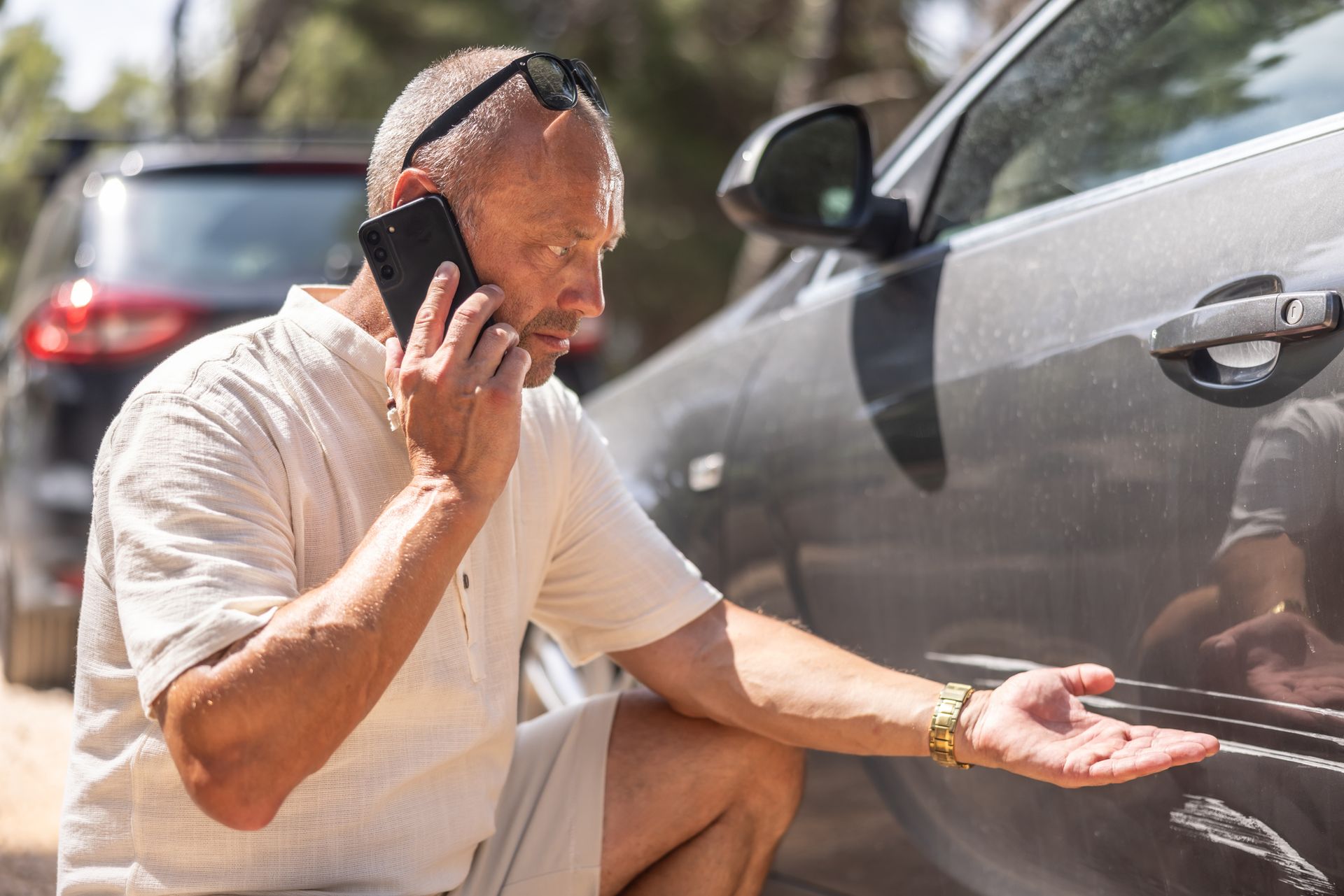 A man inspects damage on his car while calling car insurance.