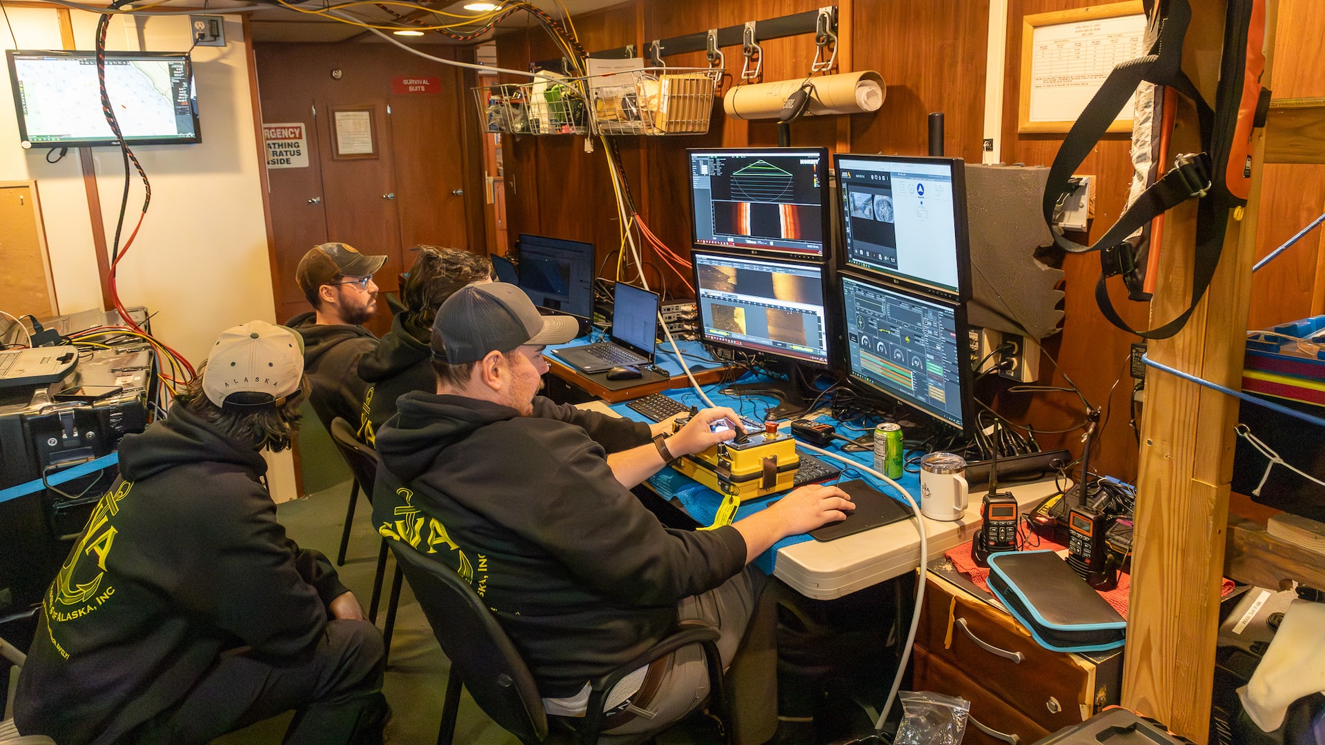 Three researchers sit in a room full of computers and controls