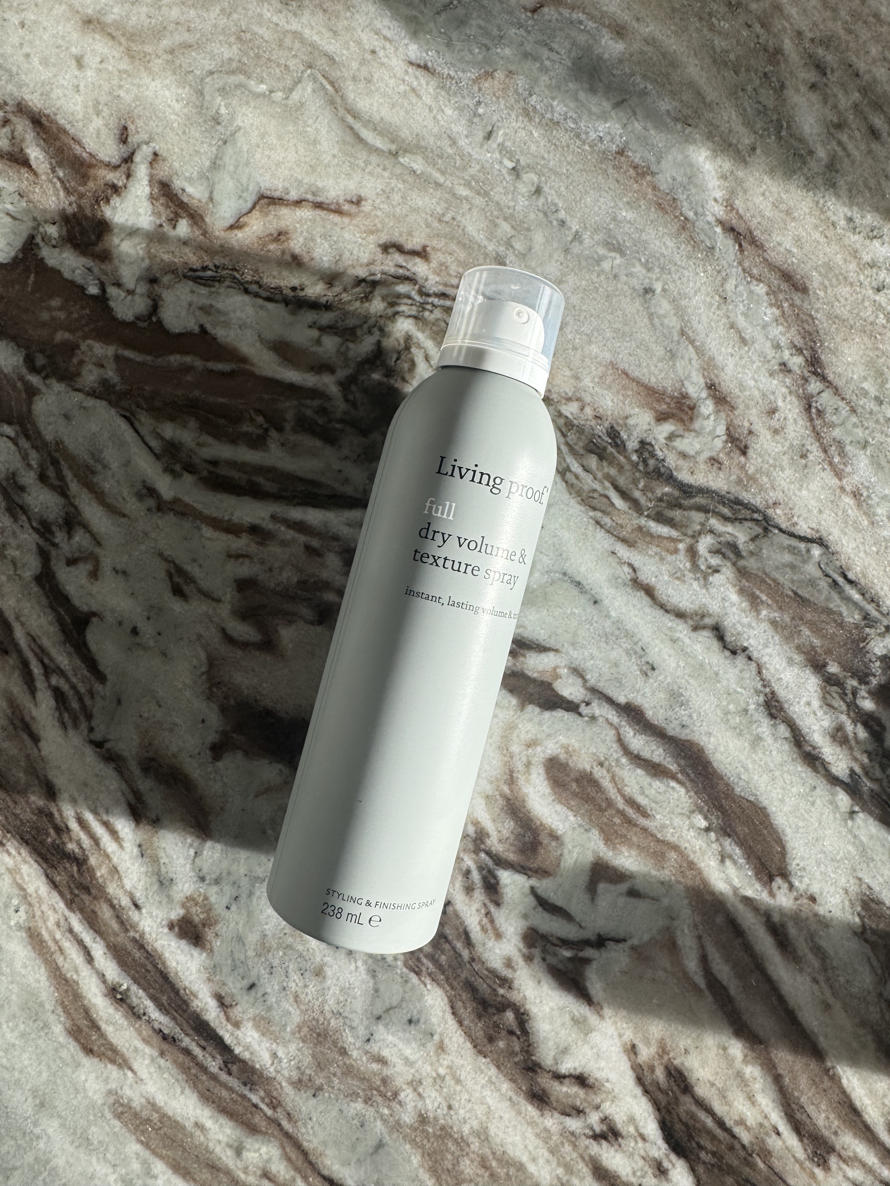 Living Proof Full Dry Volume and Texture Spray bottle on a marble surface