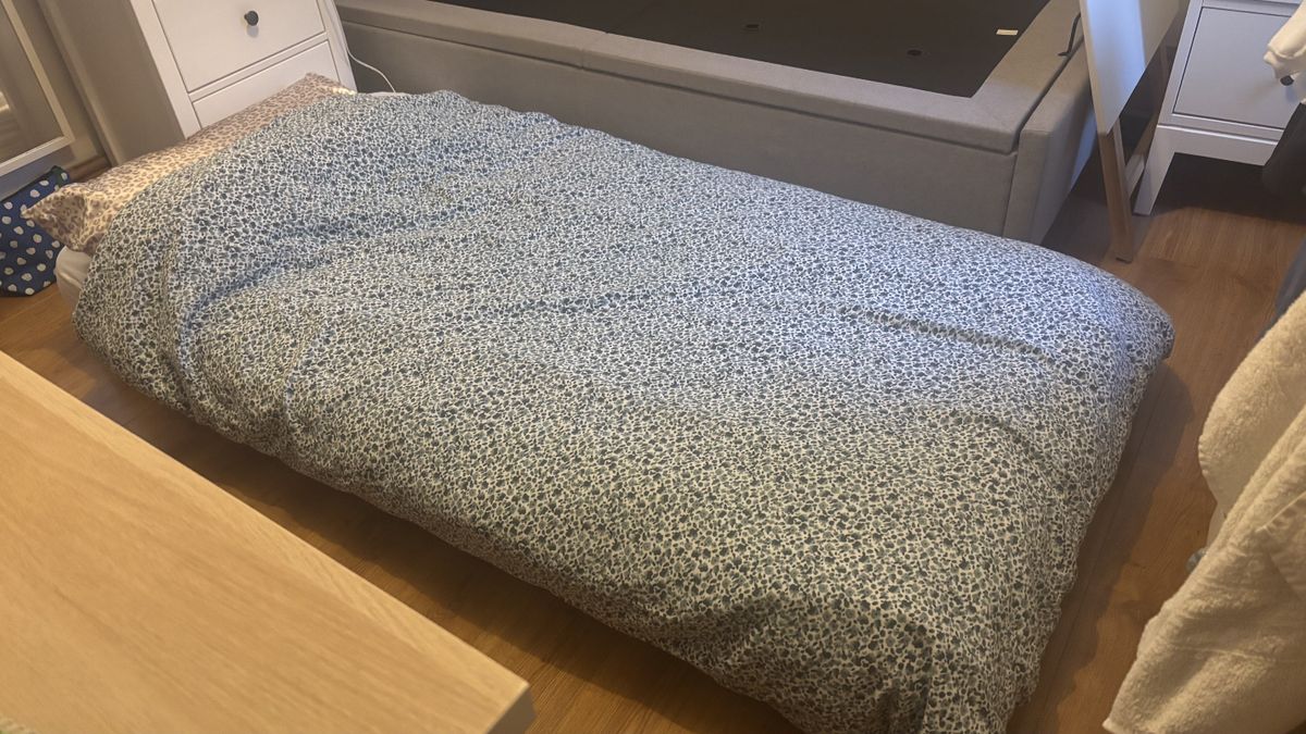 A spring mattress on the floor dressed in floral bedding.