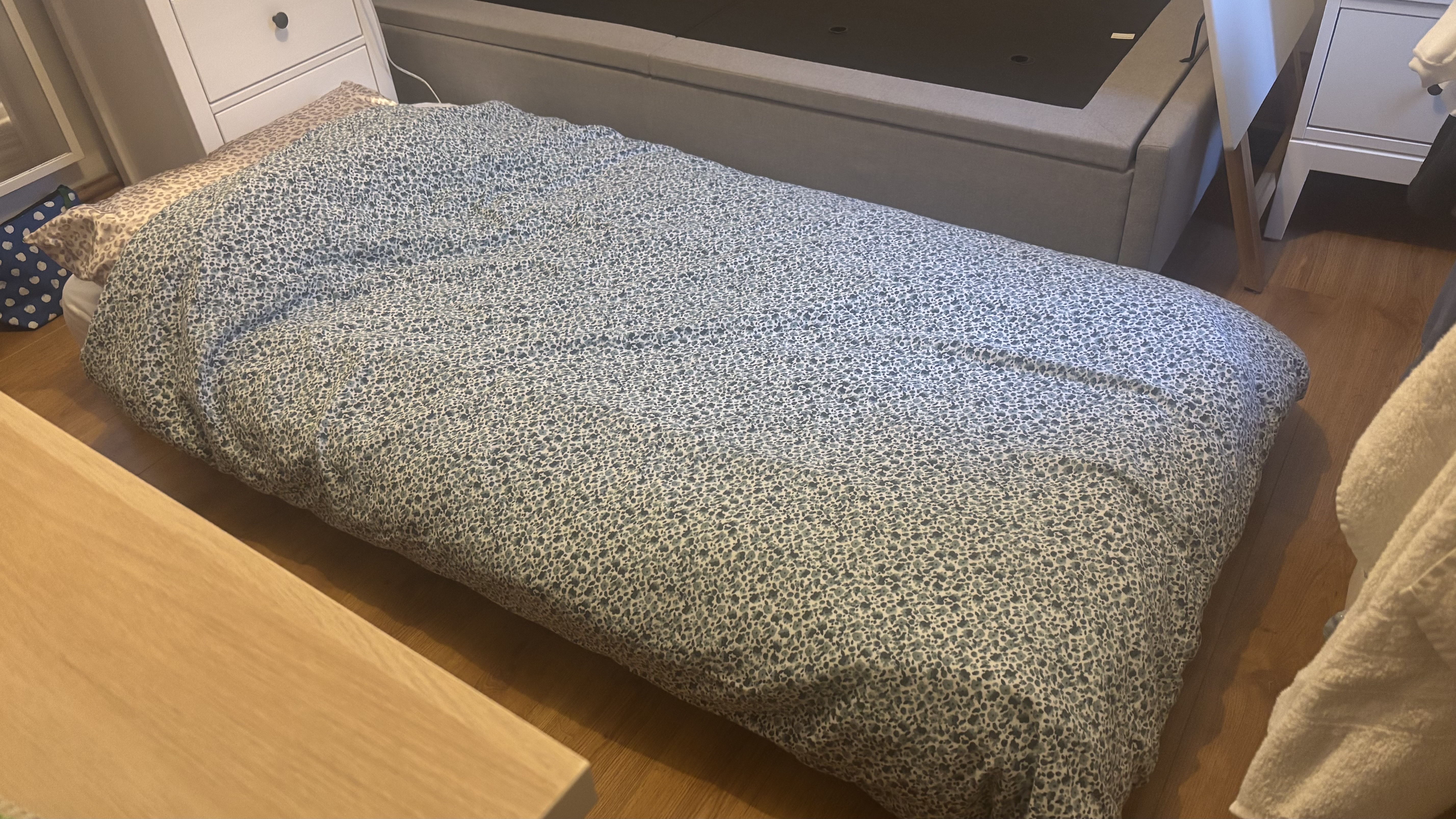 A spring mattress on the floor dressed in floral bedding.