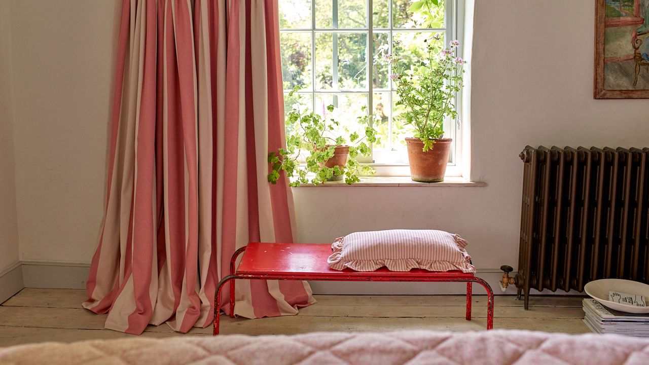 change your curtains with the seasons bedroom with red and white stripe curtains with red bench, geraniums on window sill, stripe cushion on bench, view of garden, painted floorboards, beams, bed in foreground